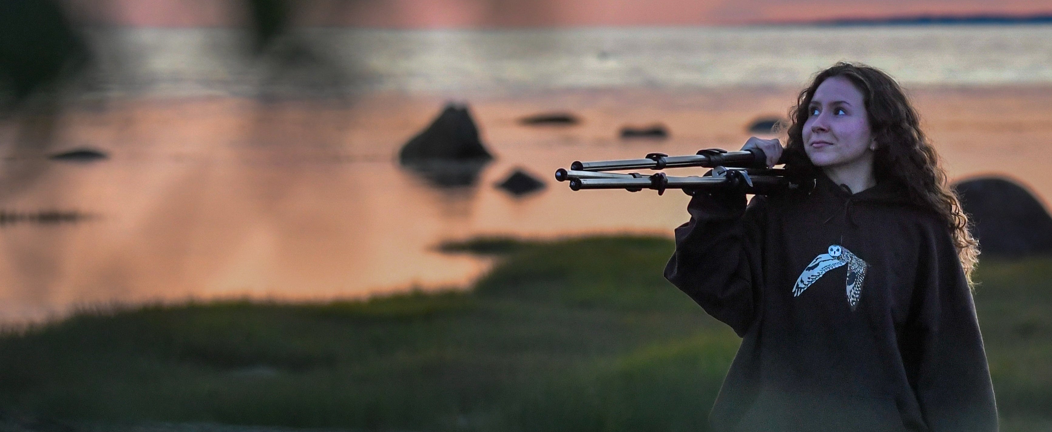 Person holding a spotting scope with a sunset or sunrise in the background