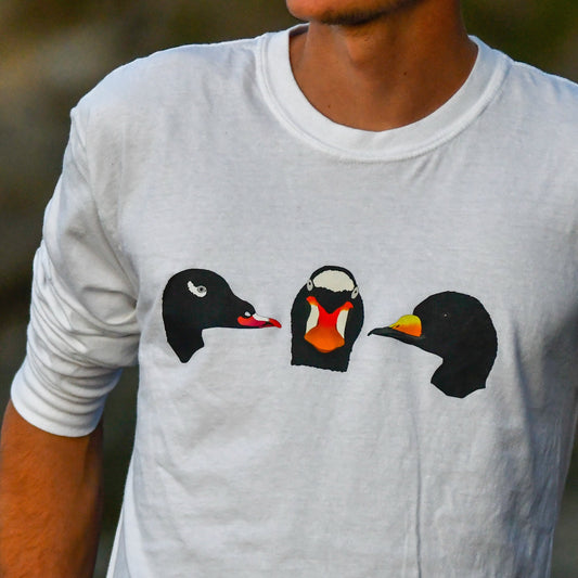 Person wearing a white t-shirt with three cartoon duck designs on a blurred natural background
