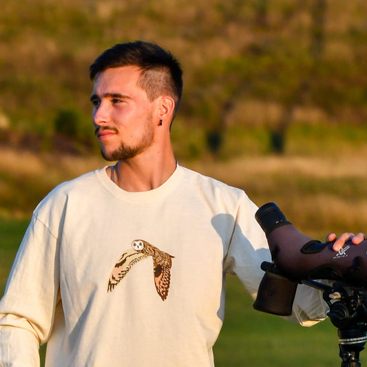 Man holding a camera with a nature-themed shirt in a field